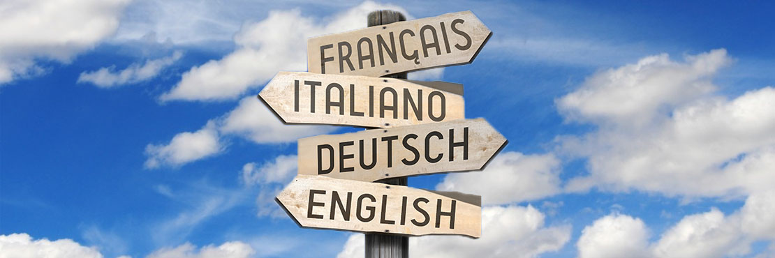 Holz-Wegweiser mit vier Pfeiler, die in verschiedene Richtungen zeigen und die Bezeichnungen «Italiano», «Deutsch», «Français» und «English» tragen..